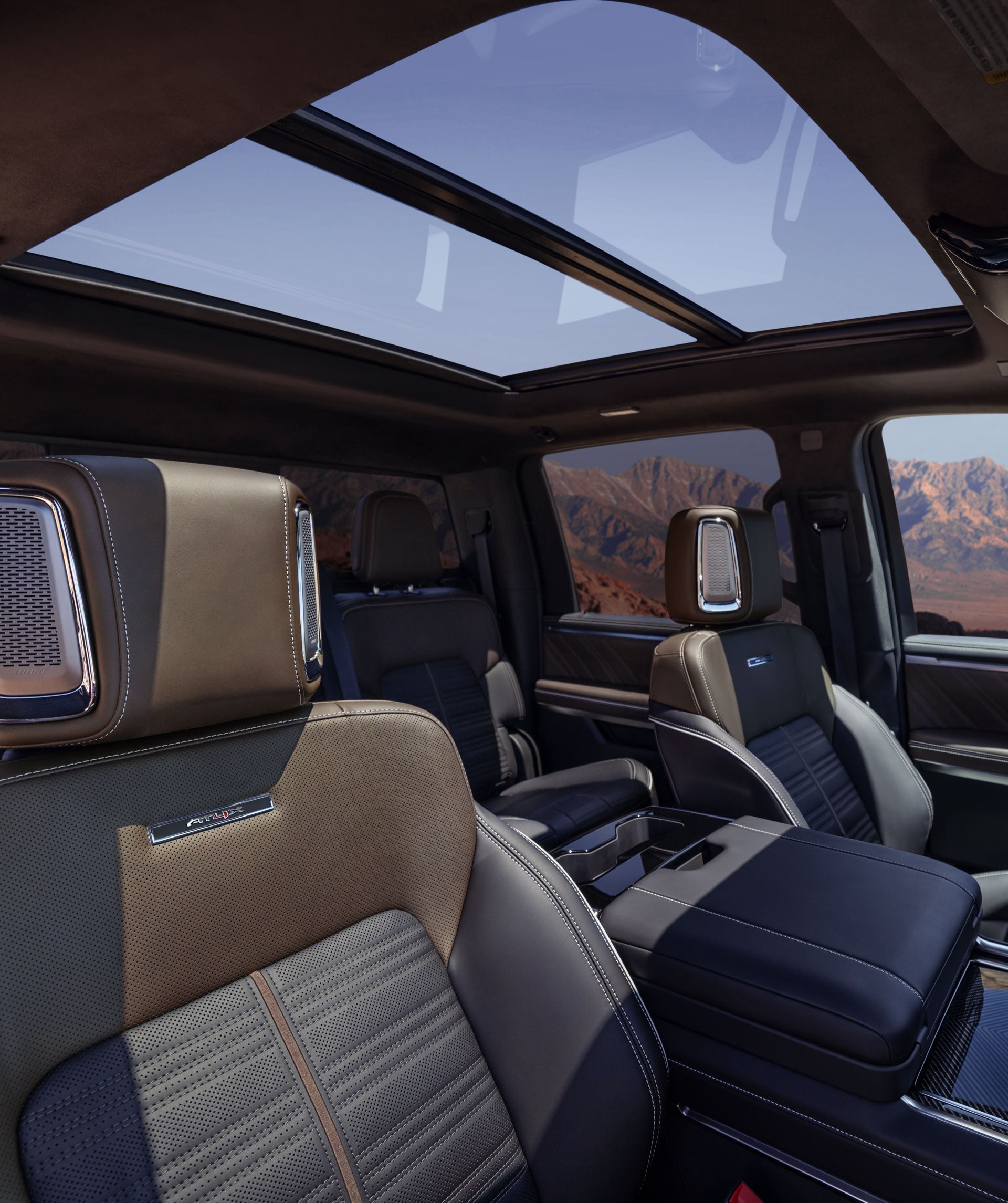 Luxurious car interior with tan and black leather seats, a panoramic sunroof, and desert mountains visible outside.